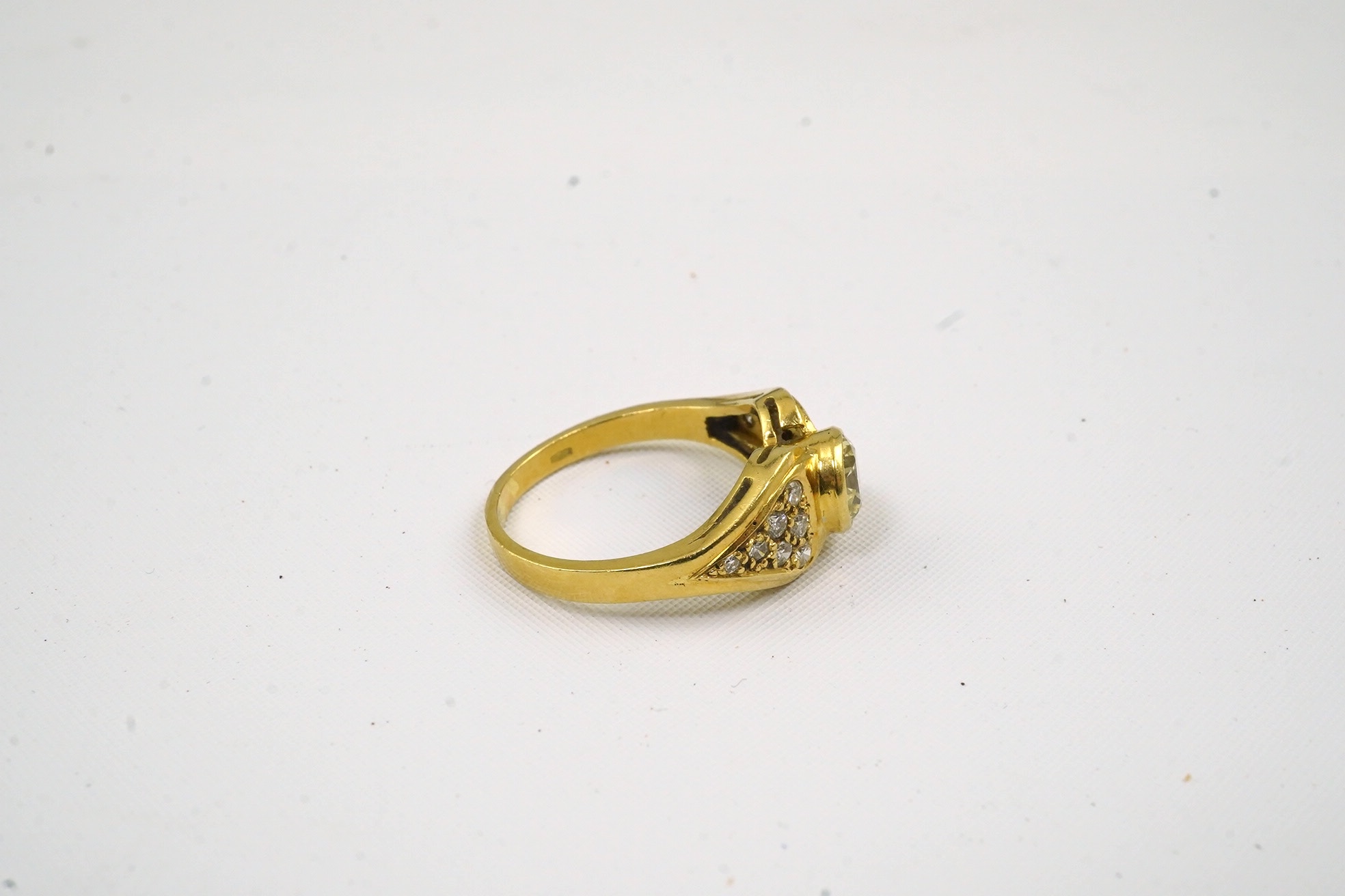 A modern 18k gold and single stone collet set diamond set ring, with fourteen stone diamond set shoulders